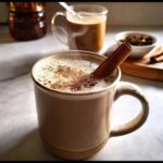 A steaming Chai Tea Latte With Warming Spices in a mug, topped with foam and cinnamon stick.