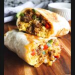 A close-up of two halves of a Savory Breakfast Burrito To Freeze, revealing scrambled eggs, seasoned meat, bell peppers, and cheese.